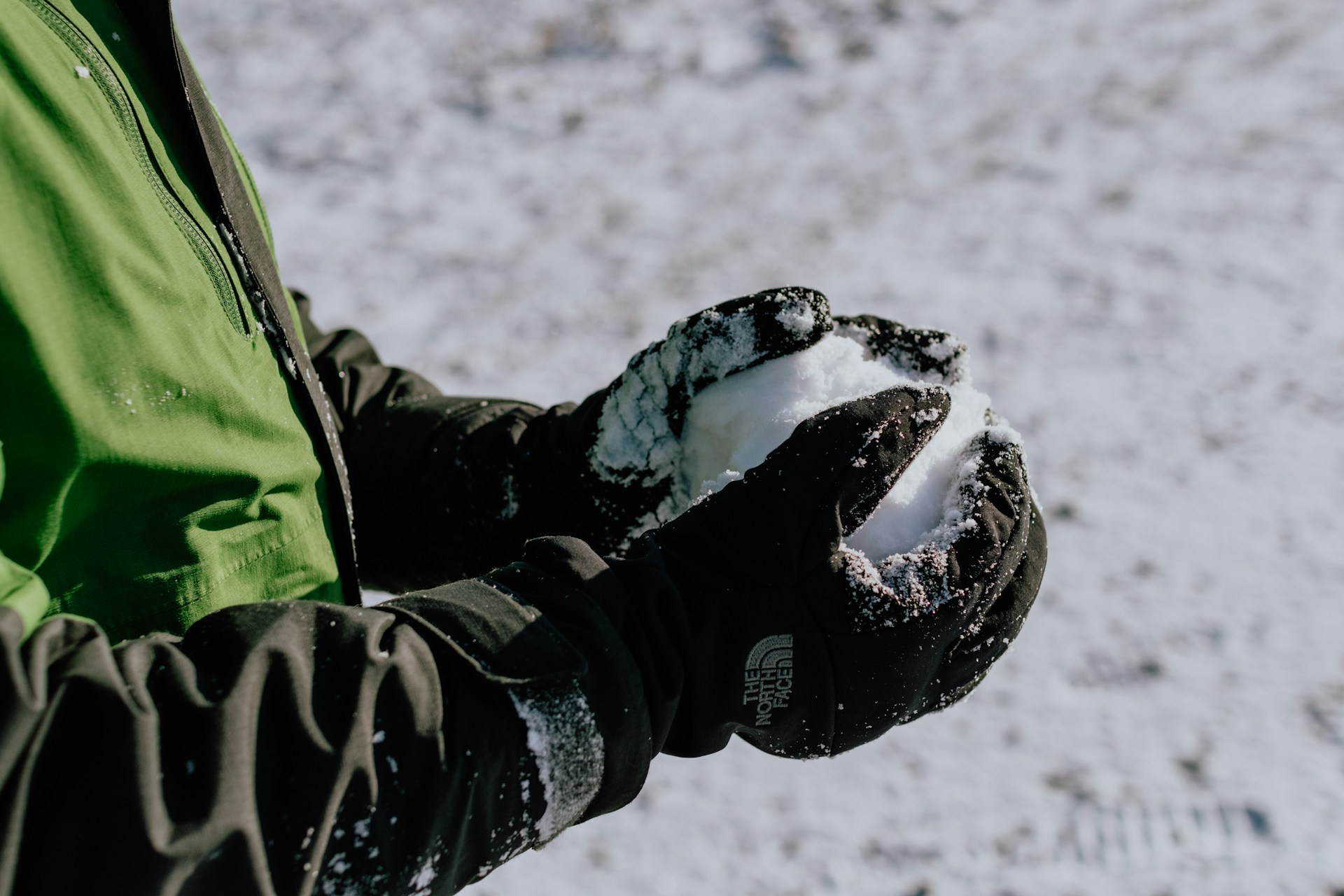 Closeup of two hands in winter gloves holding a snowball.