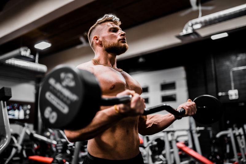 Man working out lifting weights strength training shirtless in gym