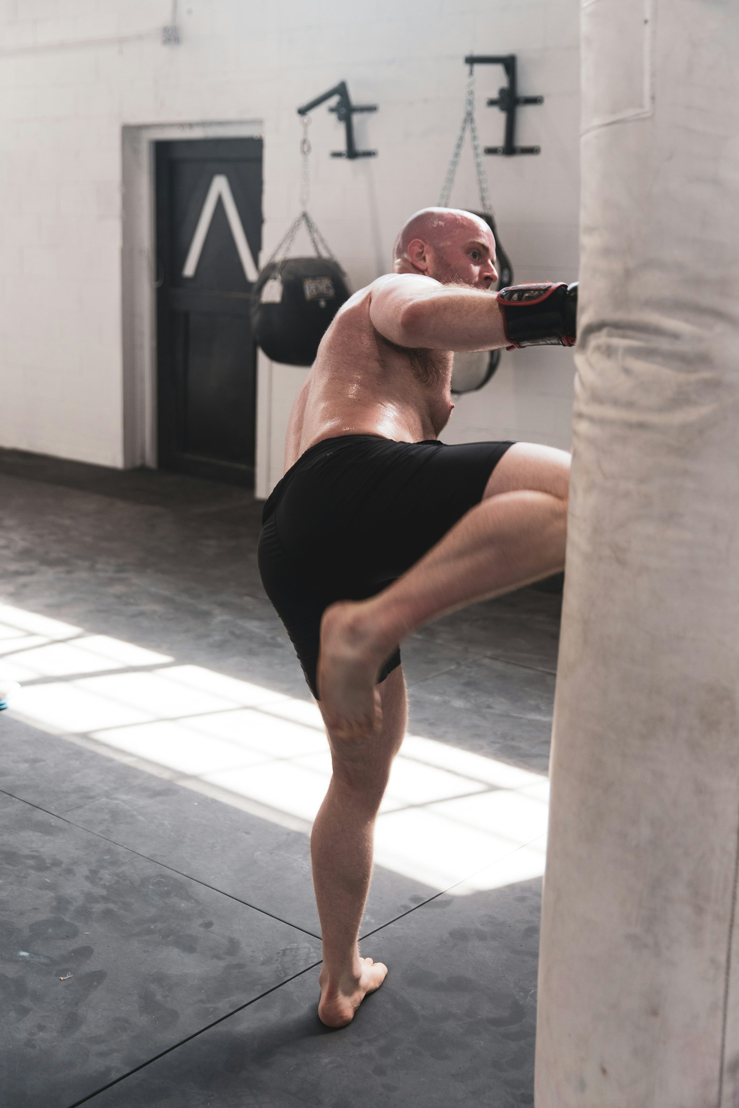 man shirtless boxing with punching bag in gym knee kick